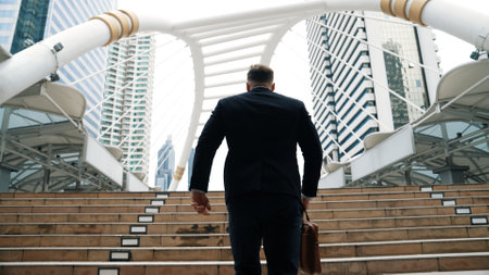 Smart caucasian businessman walking up stairs surrounded by urban view. Back view of ambitious...