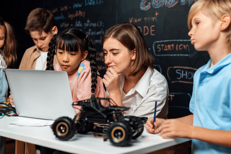 Skilled kids learning to program remote car. Schoolgirl in pink cloth use laptop for coding. Other child watch her code while teacher watch her. motherboard and electric wire also on table. Erudition.の写真素材