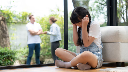 Stressed and unhappy young girl huddle in corner, cover her ears blocking sound of her parent arguing in background. Domestic violence at home and traumatic childhood depression. Panorama Synchronosの写真素材