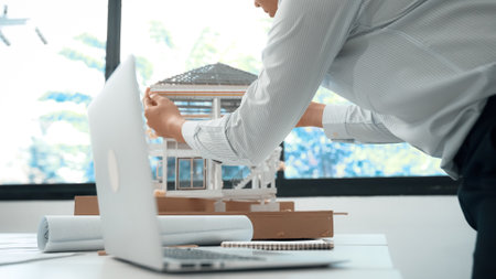 Closeup image of professional male architect engineer using laptop analysis house model structure at...