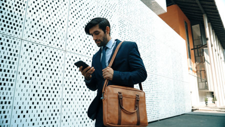 Smart manager looking at mobile phone and walking at street while wearing suit. Skilled investor looking mobile phone to checking sales or working while holding coffee cup. White background. Exultant.の写真素材