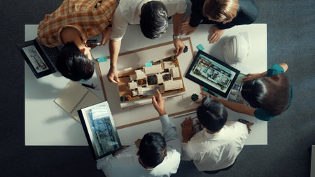 Top down view of manager pointing at house model and explain building design. Aerial view of architect engineer brainstorming about interior construction while tablet display house plan. Alimentation.の写真素材