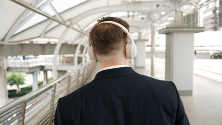 Happy business man dancing while wear headphone at bridge in urban city. Energetic manager motivation performance moving to music to celebrate successful project while walk along. Back view. Urbane.の写真素材