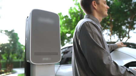 Young man recharge EV electric car in green sustainable city outdoor summer garden as lifestyle of...