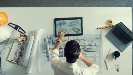 Top view of skilled architect looking at project plan at tablet. Aerial view of civil engineer planning while checking building blueprint at meeting room with safety helmet and laptop. Alimentation.の写真素材