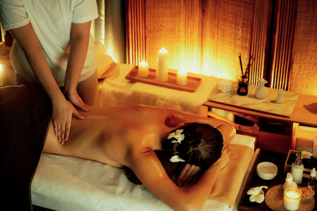 Caucasian woman customer enjoying relaxing anti-stress spa massage and pampering with beauty skin recreation leisure in warm candle lighting ambient salon spa at luxury resort or hotel. Quiescentの写真素材