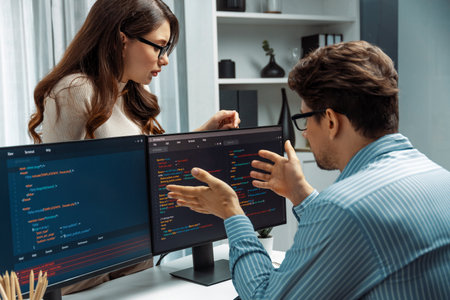 Woman colleague standing opposite to man programmer working on desk to discuss coding website...