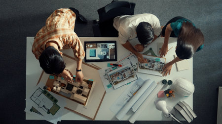 Top view of project manager working together to brainstorm house design while standing around meeting table with project plan and blueprint. Aerial view of designer team explain project. Alimentation.の写真素材