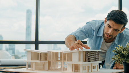 Smart caucasian engineer or project manager measure check, inspect, look at house model while standing near panorama window with city, skyscraper view. Manager design house construction. Traceryの写真素材