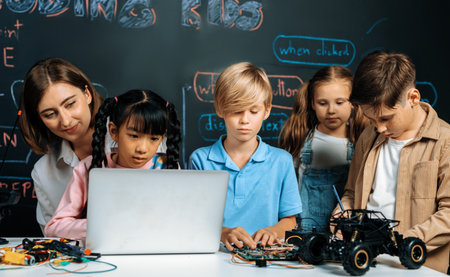 Skilled kids learning to program remote car. Schoolgirl in pink cloth use laptop for coding. Other child watch her code while teacher watch her. motherboard and electric wire also on table. Erudition.の写真素材