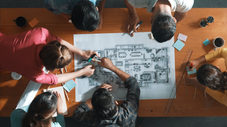 Top down of skilled business people holding tablet an looking at blueprint. Aerial view of architect...