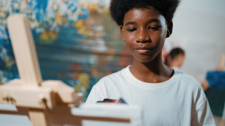 Closeup of african boy hand paint canvas with warm tone color while caucasian girl in casual outfit drawing cool tone colors behind at colorful stained wall. Creative activity concept. Edification.の写真素材