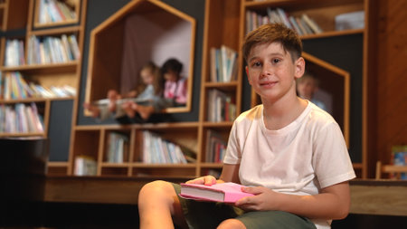 Caucasian boy looking at camera while group of smart students sitting at library. Child studying,...