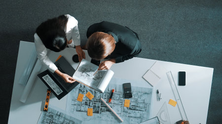 Top view of businesswoman hand blueprint to engineer sitting at meeting table with project plan, equipment and safety helmet. Aerial view of manager explain about building construction. Alimentation.の写真素材