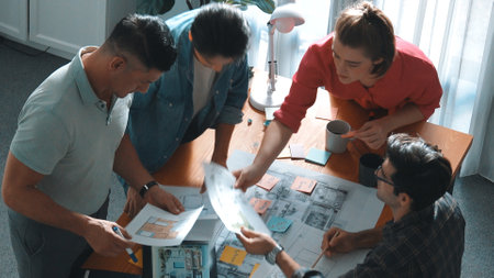 Top down of skilled business people holding tablet an looking at blueprint. Aerial view of architect engineer planning and design house design together while standing at table with laptop. Symposium.の写真素材