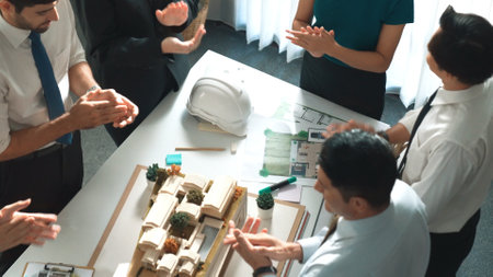 Top view of team clapping hands to celebrate project at meeting table with house model, architectural document and safety helmet. Smart project manager applause to successful project. Alimentation.の写真素材