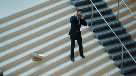 Professional business man standing at stair while moving to music from headphone. Skilled project manager dancing while listening relax sound with laptop placed on stairs. Modern dance. Exultant.の写真素材