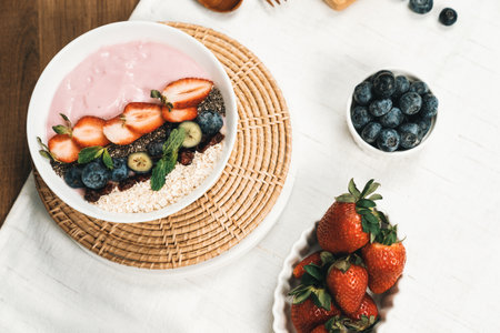 Presented by fruits putting yogurt toppings with strawberry, berry, oats, raisins and chia seed decorated by peppermint in white blow. Pink background. Set of healthy dairy product choice. Pecuniary.の写真素材