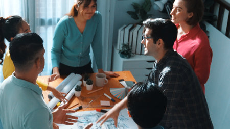Top view of civil engineer team writing at blueprint at meeting table with color palettes. Group of...