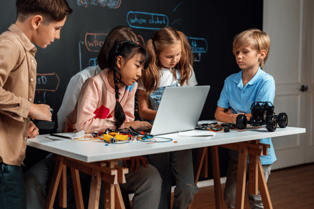 Skilled kids learning to program remote car. Schoolgirl in pink cloth use laptop for coding. Other child watch her code while teacher watch her. motherboard and electric wire also on table. Erudition.の写真素材
