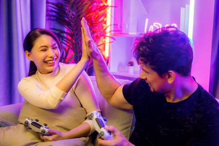 Couple joyful of player video game on TV using joysticks making high five of winner together on...
