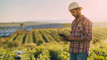 A man in a natural landscape holds a tablet while a drone hovers in the sky above a grassland with windmills and plants. AIG41の素材