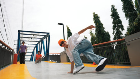 Panorama shot of professional hipster perform b-boy performance and energetic footstep. Skilled happy man practice break dance while friend cheering him at bridge. Outdoor sport 2024. Sprightly.の写真素材