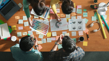 Top down aerial view of skilled designer hold logo while discuss with team. Aerial business group working together sharing idea about logo graphic design by using sticky notes and tablet. Symposium.の写真素材