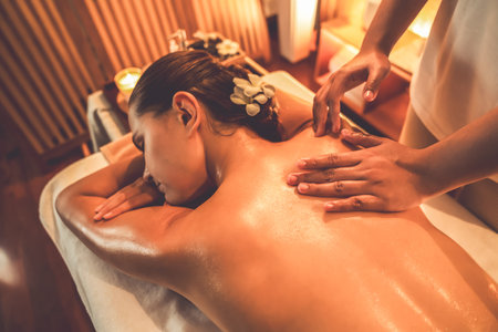 Caucasian woman customer enjoying relaxing anti-stress spa massage and pampering with beauty skin recreation leisure in warm candle lighting ambient salon spa at luxury resort or hotel. Quiescentの写真素材