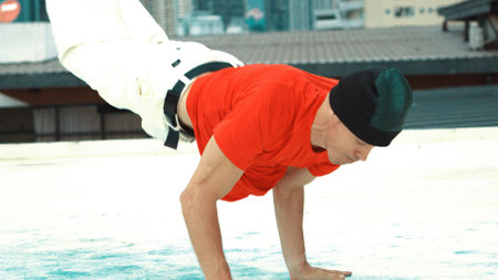 Professional break dancer doing head spin at roof top with city view. Group of caucasian hipster...