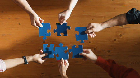 Top down view of skilled business people separated blue jigsaw puzzle on meeting table. Group of...