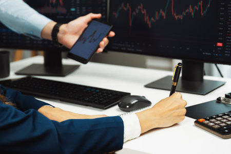 Cropped pointing hand with pen in businessman, checking with holding smartphone by woman investor online website program application with dynamic stock market at home office at back side. Infobahn.の写真素材