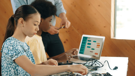 Teacher standing while explain coding and robotic construction. Diverse teenager fixing mother board and using electronic tool while looking at laptop display programing code screen. Edification.の写真素材