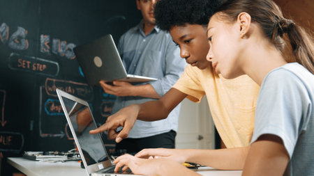 Caucasian girl programing or coding system while african boy fixing model. Teacher holding laptop while looking at diverse children writing web develop program. Innovation education. Edification.の写真素材