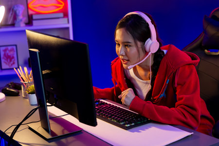 Host channel of beautiful Asian girl streamer concentrating online game wearing headphones pastel...