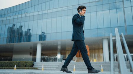 Smart business man using phone to talking while walking at building. Happy manager walking at street while talking on smart phone to discuss business plan or marketing strategy or working. Exultant.の写真素材