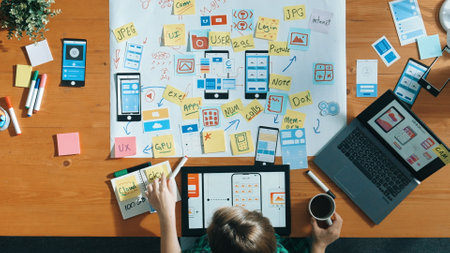 Top view of smart developer working on tablet and writing Ux Ui design for mobile phone interface at...