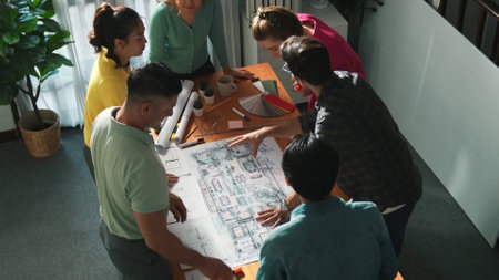 Top view of civil engineer team writing at blueprint at meeting table with color palettes. Group of...