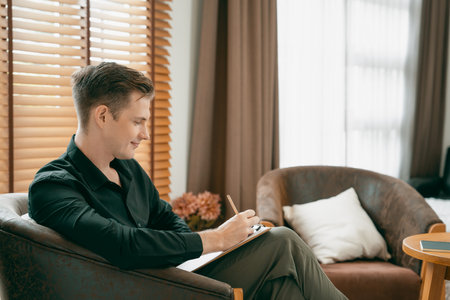 Portrait of happy and smiling male psychologist portrait sitting on arm chair in psychiatrist office or therapy room. Friendly and professional mental healthcare counselor and therapist. Unveilingの写真素材
