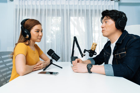 Smiling radio influencer host wearing headphone interviewing woman speaker sharing information to listeners on social media online website live streaming channel at morning at studio record. Infobahn.の写真素材