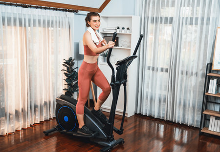 Athletic and sporty woman running on elliptical running machine during home body workout exercise...