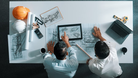 Top view of skilled civil engineer working together to plan building design. Top down aerial view of skilled architect team sitting at table while manager using tablet open project plan. Alimentation.の写真素材