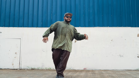 Hipster dancing b-boy foot step at street with blue wall. Asian break dancer practice street dance...