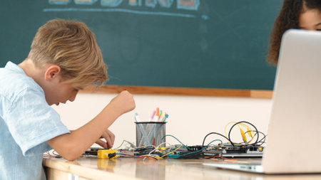 Diverse smart student working together to fix main board at stem class while looking at laptop...