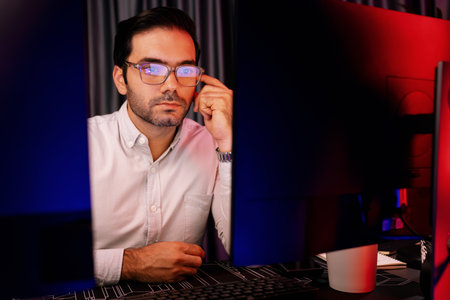 Smart businessman wearing glasses, concentrating on dynamic stock exchange investment on two pc screens at neon light office in dark room night with high profit in searching research market. Surmise.の写真素材