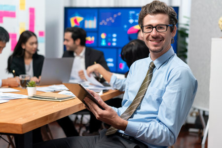 Portrait of businessman or analyst looking at camera with his colleague analyzing data analysis in...