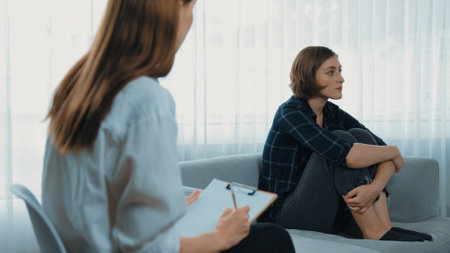 Sad PTSD woman patient in therapy for mental health with psychologist, depression or grief after life failure. Frustrated trauma young woman talking to prim psychologist about emotion in clinicの写真素材