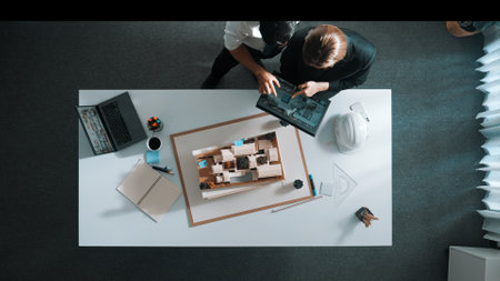 Top down view of manager pointing at house model and explain building design. Aerial view of...