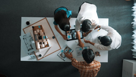 Top down view of architect engineer team discussing and point at tablet display construction at table with blueprint and house model at meeting. Diverse designer planning design house. Alimentation.の写真素材