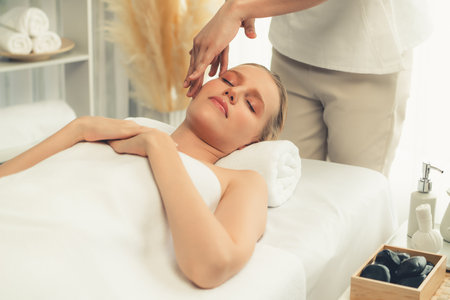 Caucasian woman enjoying relaxing anti-stress head massage and pampering facial beauty skin recreation leisure in dayspa modern light ambient at luxury resort or hotel spa salon. Quiescentの写真素材